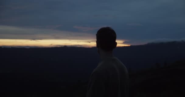 Tiro estático de um macho branco no topo da colina durante o pôr do sol olhando ao redor no escuro. — Vídeo de Stock
