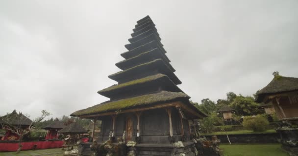 Κοντινό πλάνο χαμηλού επιπέδου κυκλώνοντας γύρω από ένα θρησκευτικό κτίριο παγόδα στο ναό Besakih στο Μπαλί, Ινδονησία Εκπληκτική παγόδα καλυμμένη με γρασίδι σε μια συννεφιασμένη μέρα — Αρχείο Βίντεο
