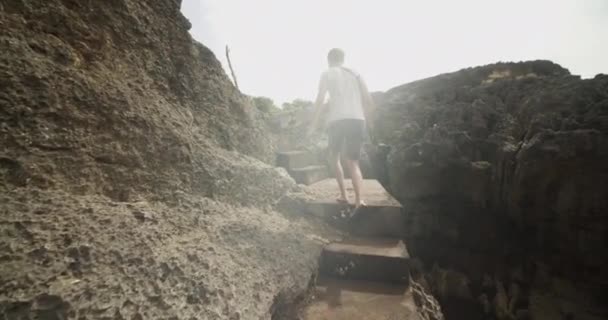 Seguendo un uomo che sale le scale di pietra sulla scogliera rocciosa vicino all'oceano Turista maschile che sale le scale vicino a Broken Beach Pasih Uug a Bali Indonesia — Video Stock