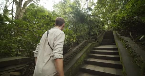 Jongeman in kaki kleren klimmend de trap op in een oude tempel in de Bali jungle. Blanke man loopt de stenen trap op in de jungle. — Stockvideo