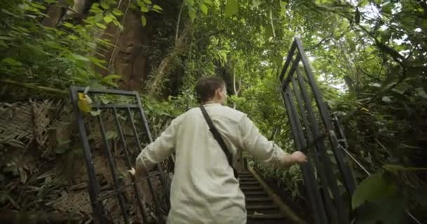 Követve a pov lövés fiatal fehér férfi sétál át a vas kapuk egy ősi romok és körülnézett a dzsungelben Balin. — Stock videók