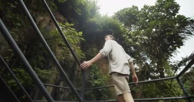 Genç bir erkek kâşifin tropikal yağmur ormanlarında demir korkuluklarla merdivenlerden çıkışını takip eden alçak açılı çekim.