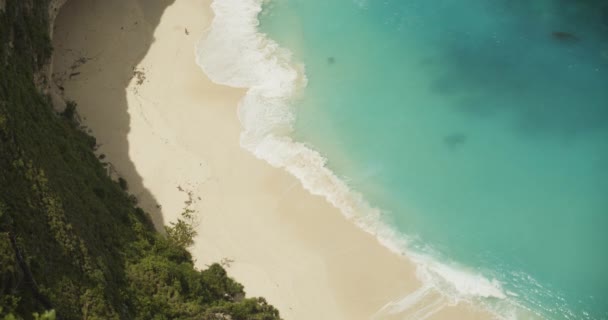 青い波が砂の熱帯のビーチに衝突し、ゆっくりとした動きを閉じる｜ターコイズブルーの熱帯の海とバリの砂のビーチの景色を見下ろす — ストック動画