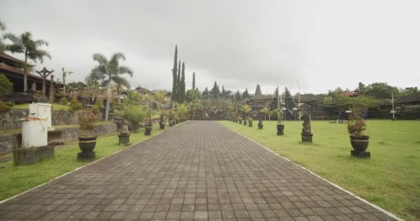 Lente photo de poupée de marcher sur la route pavée entourée de belles statues de pierre sur le terrain du temple Besakih à Bali — Video