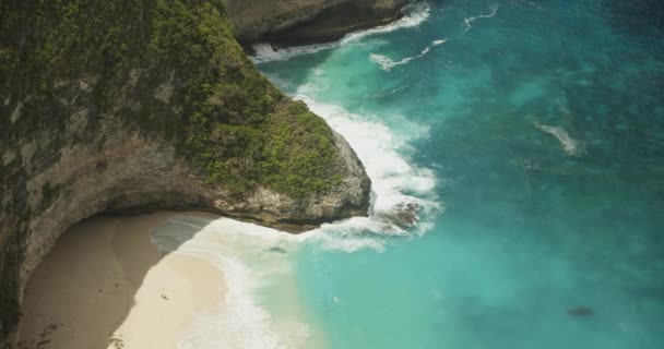 在热带岩石悬崖峭壁和沙滩上，拍下了慢镜头的蓝色海浪冲撞在热带岩石悬崖峭壁和沙滩上俯瞰着热带绿松石海洋、热带植被悬崖峭壁和巴厘岛沙滩 — 图库视频影像