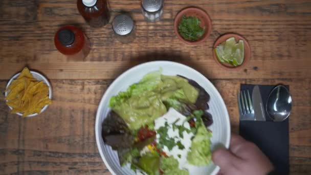 Sopra la testa della tradizionale insalata messicana nella ciotola posta sul tavolo di legno servito. Verdure fresche e salsa in una ciotola posta accanto a una ciotola di tortilla, lime e prezzemolo — Video Stock