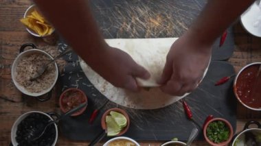 Masada geleneksel Meksika mutfağından burrito yapıyorum. Masadaki yemek hazırlıklarına yukarıdan bak. Dürümü yarıya indirip paketliyorum.