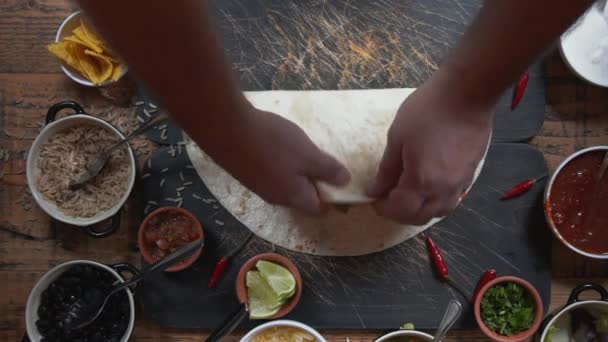 テーブルの上に伝統的なメキシコ料理の料理ブリトーを作る。テーブルの上に食べ物の準備のトップダウンビュー。半分に包みブリトーを切る — ストック動画