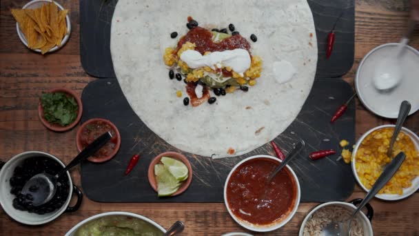 Überblick über das Hinzufügen von Zutaten zu Tortilla und die Herstellung eines Burrito. Blick von oben auf das Hinzufügen von frischem Gemüse, Soßen und Kräutern in Tortilla und das Einwickeln. Burrito halbieren — Stockvideo