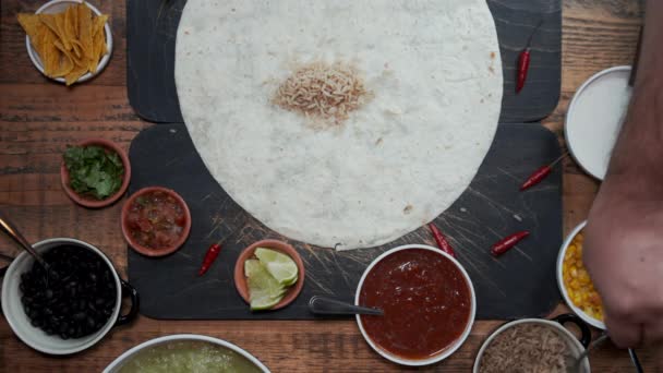 Pohled shora na ruku připravující tortilla přidáním různých čerstvých zdravých složek. Shora dolů pohled na výrobu mexického stylu burrito s čerstvou zeleninou, salsa omáčka rýže a fazolí — Stock video