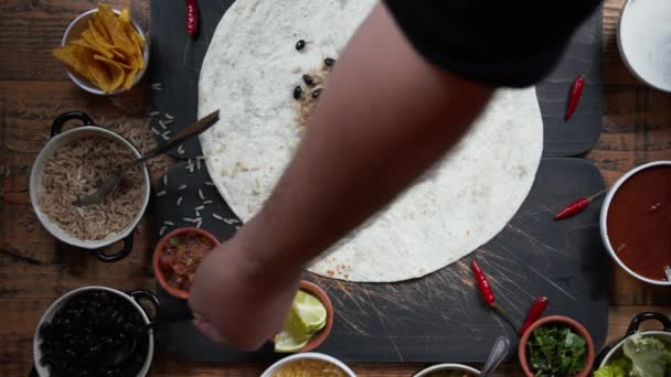 Widok z góry na robienie burrito. Dodawanie mięsa, salsy, ziół i świeżych warzyw do tortilli i podejmowania tradycyjnych dań kuchni meksykańskiej. Widok ogólny na przygotowanie żywności — Wideo stockowe
