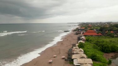 Yağmur mevsiminde Canggu, Bali 'deki kumsaldaki insanlar. Yerel halkın fırtınadan önce plajda dinlenip okyanusta yüzüşünü gösteren hava manzarası.
