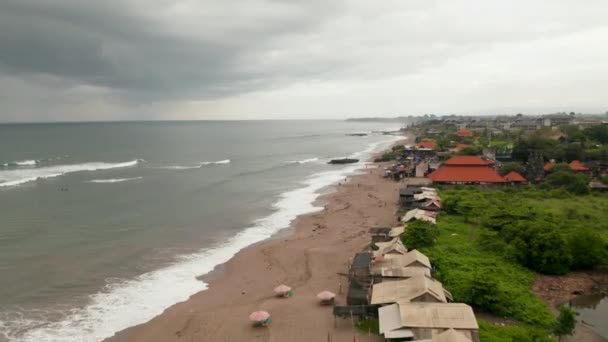 Persone sulla spiaggia di sabbia a Canggu, Bali durante la stagione delle piogge. Veduta aerea della gente locale che si rilassa sulla spiaggia e nuota nell'oceano prima della tempesta — Video Stock