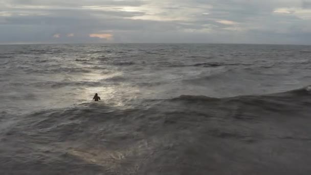 Mężczyzna siedzący wieczorem na desce surfingowej na wzburzonym morzu. Surfer siedzi na desce surfingowej podczas zachodu słońca na Bali — Wideo stockowe