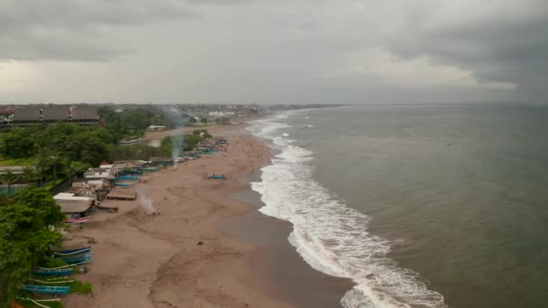 Pessoas relaxando em uma praia de areia tropical antes da tempestade em Canggu, Bali. Vista aérea dolly de barcos coloridos e turistas na famosa praia turística na Indonésia — Vídeo de Stock