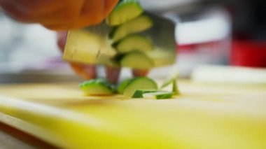 Yeşil salatalığı küçük parçalara ayırmak. Yeşil sebzeleri çabucak kesen bir aşçının yakın görüntüsü