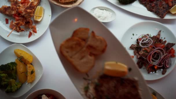Pohled shora na ruku podávající maso a grilovaný chléb na bílém talíři. Horní pohled na stůl s více předkrmy talíře v luxusní restauraci — Stock video