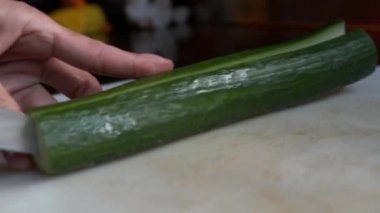 Salatalığı boydan boya kesen bıçağın yakın görüntüsü. Kesme tahtasında sebze hazırlama ve çekirdek çıkarma