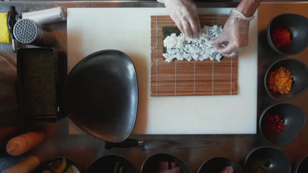 Visão de cima para baixo do chef profissional fazendo sushi. Visão geral do cozinheiro adicionando arroz, legumes e especiarias no rolo de sushi — Vídeo de Stock