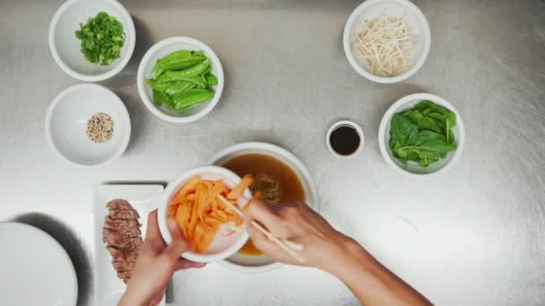 Blick von oben auf die Herstellung traditioneller asiatischer Gemüse- und Fleischnudelsuppe von Grund auf. Blick von oben auf die Zugabe verschiedener Zutaten von Schüsseln zur Nudelsuppe — Stockvideo