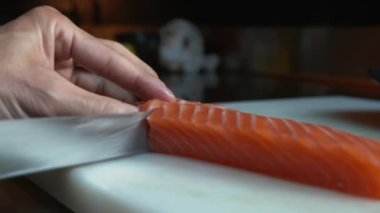 Somonu ince dilimlere ayıran bıçaklı bir elin yakın görüntüsü. Kesme tahtasında kırmızı balığı ince ince dilimlemek.