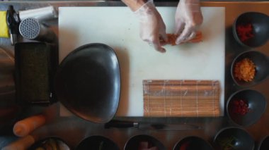 Restoranda suşi yapan aşçının genel manzarası. Profesyonel şefin suşiye somon ekleyip küçük parçalara ayırdığı tepeden tırnağa bir manzara.