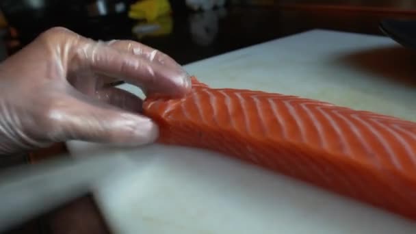 Corte de salmão em fatias finas. Cozinhe em luvas de proteção cortando peixe vermelho com faca em pedaços finos — Vídeo de Stock
