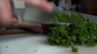 Bıçağın çok sayıda soğanı küçük sebze parçalarına ayırmasını yakından izleyin. Mutfak masasında yeşil sebze hazırlıyorum.