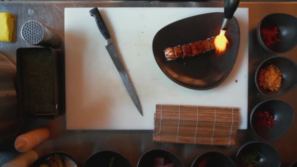 Vista de arriba hacia abajo del chef profesional que calienta sushi con una pistola de calor. Vista aérea de cocinar salmón encima del sushi con una pistola de calor — Vídeos de Stock