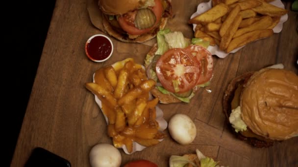 Τηγανητές πατάτες και μπιφτέκια σε ξύλινο τραπέζι. Overhead πάνω προς τα κάτω άποψη των διαφόρων fast foods που εμφανίζονται στο τραπέζι — Αρχείο Βίντεο