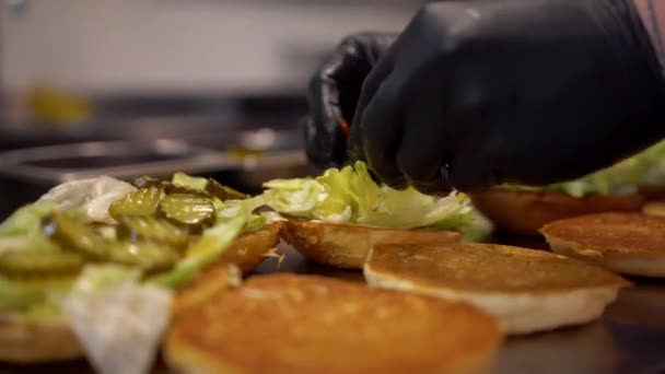 Ετοιμάζω μπιφτέκια σε φαστφουντάδικο. Close up άποψη ενός εργάτη fast food προσθέτοντας λαχανικά στο burger — Αρχείο Βίντεο