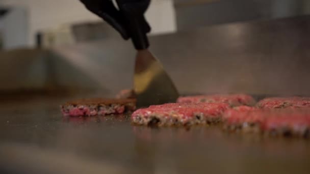 レストランキッチンのホットプレートに肉パテを反転させます。ファーストフードレストランでヘラでハンバーガーの肉を反転プロの料理のビューを閉じます — ストック動画