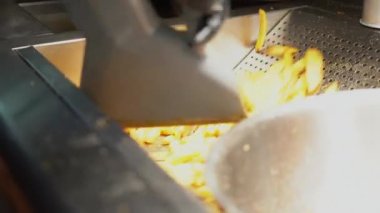 Fast food mutfağında patates kızartması yapmak. Eldivenli ve tuzlu patates kızartmalı fast food işçisinin yakın görüntüsü.