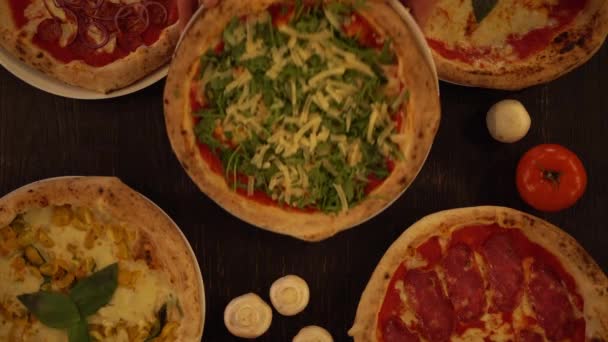 Het serveren van vers gemaakte arugula en kaas pizza op een houten tafel. Overhead top down zicht van het assortiment van verschillende pizza 's op een houten tafel — Stockvideo