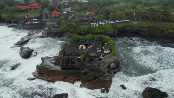 Inclinazione tiro aereo volando via dal tempio vuoto Tanah Lot durante il tempo pericoloso a Bali, Indonesia. Pericolose onde del mare che si infrangono su rocce scure con il famoso tempio indù — Video Stock