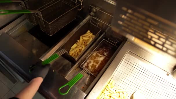 Sült krumpli olajban a gyorsétterem konyhájában. A gyorséttermi munkás felülnézeti nézete, amint sült krumplit csinál egy kereskedelmi sütőben — Stock videók