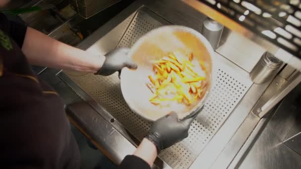 Trabalhador de fast food a fazer uma porção de batatas fritas. Visão geral do trabalhador de fast food adicionando sal à porção de batatas fritas na cozinha — Vídeo de Stock