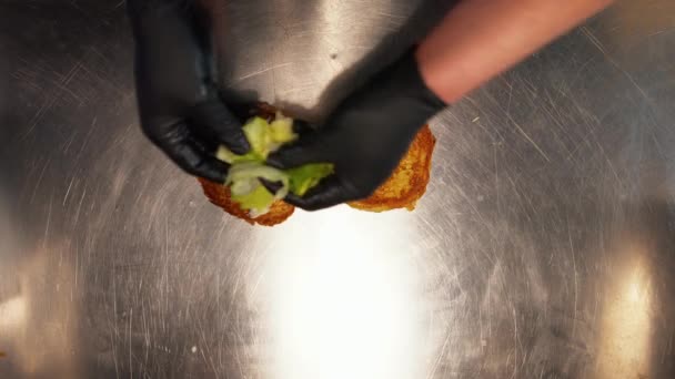 Pohled shora dolů, jak dělník dělá hamburger. Pohled shora na zaměstnance restaurace v rukavicích přidávajících maso, zeleninu a majonézu do hamburgerové housky — Stock video