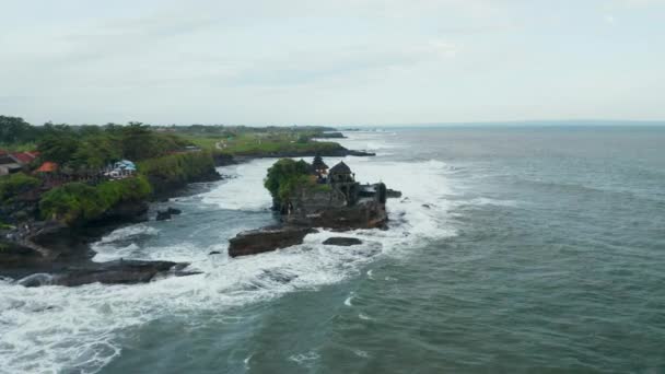Brede luchtfoto van geïsoleerde lege Tanah Lot tempel tijdens gevaarlijk weer. Sterke golven storten neer in donkere rotsachtige klif met beroemde Hindoe tempel in Bali, Indonesië — Stockvideo