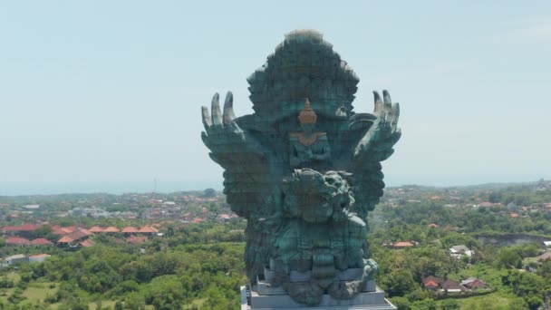 Draaiend vooraanzicht van majestueus koperen en koperen Garuda Wisnu Kencana standbeeld in Bali, Indonesië. Groot blauw groen standbeeld dat boven de woonhuizen uitsteekt — Stockvideo