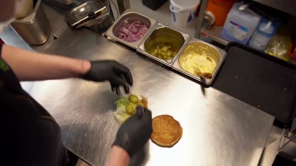 Visão aérea do trabalhador de fast food fazendo hambúrguer em um restaurante de fast food. Visão de cima para baixo da preparação de hambúrguer com legumes, carne e molhos — Vídeo de Stock