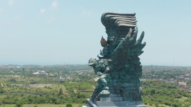 Luchtopname rond het Garuda Wisnu Kencana standbeeld in Bali, Indonesië. Beroemd religieus standbeeld met woonwijken op de achtergrond — Stockvideo