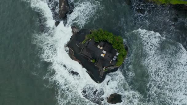 小さな岩の崖の上にタナロット寺の上空からの眺め。インドネシアのバリ島で強い波が吹く小さな島で有名なヒンズー教の寺院のドルリーへのトップダウン傾斜 — ストック動画