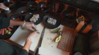Profesyonel şef avokado dilimlerinin içinde pirinç topları yuvarlıyor. Bir restoranda suşi yemeği için sebze sosu hazırlarken yukarıdan aşağı bakan bir manzara.