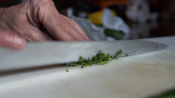 Vista de perto de cortar cebolinha em pequenos pedaços. Preparando legumes verdes na mesa da cozinha — Vídeo de Stock