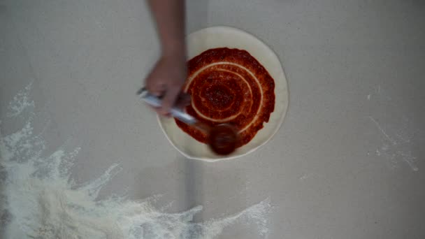 Top down view of a chef making pizza on countertop with flour. Overhead view of professional cook putting ketchup and salami on pizza dough on the table — Vídeo de stock