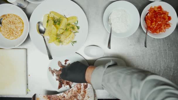 Fast food worker σερβίρει και καρυκεύματα κομμάτια κρέατος για το παραδοσιακό πιάτο της Μέσης Ανατολής κεμπάπ. Προσθήκη βοτάνων, λαχανικών και κρεμμυδιών σε κομμάτια κρέατος στο πιάτο — Αρχείο Βίντεο