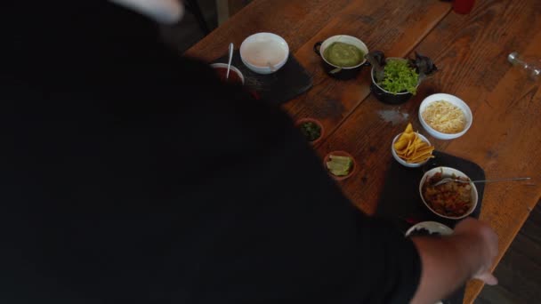Cook adding ingredients to traditional Mexican burrito bowl dish. Man adding ingredients into the bowl. Fresh salsa, herbs, vegetables, rice and beans added to the dish on the table — Vídeos de Stock