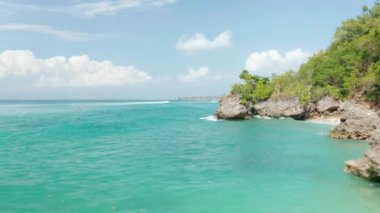 Endonezya, Bali 'de lüks villaları olan sarp kayalıklardaki tropikal mavi okyanusta sörfçülerin alçak hava manzarası