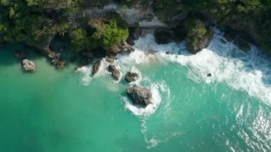 Mavi dalgalar tropik kıyı şeridine çarpıyor. Kayalık kayalıkların etrafında köpüren turkuaz mavi su manzarası